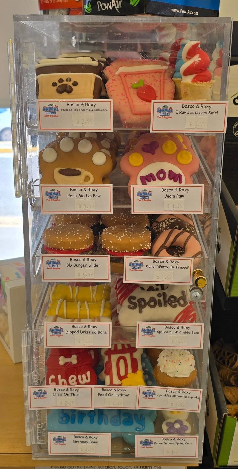 A clear display case of decorated dog-bakery treats, cookies and donut-shaped biscuits