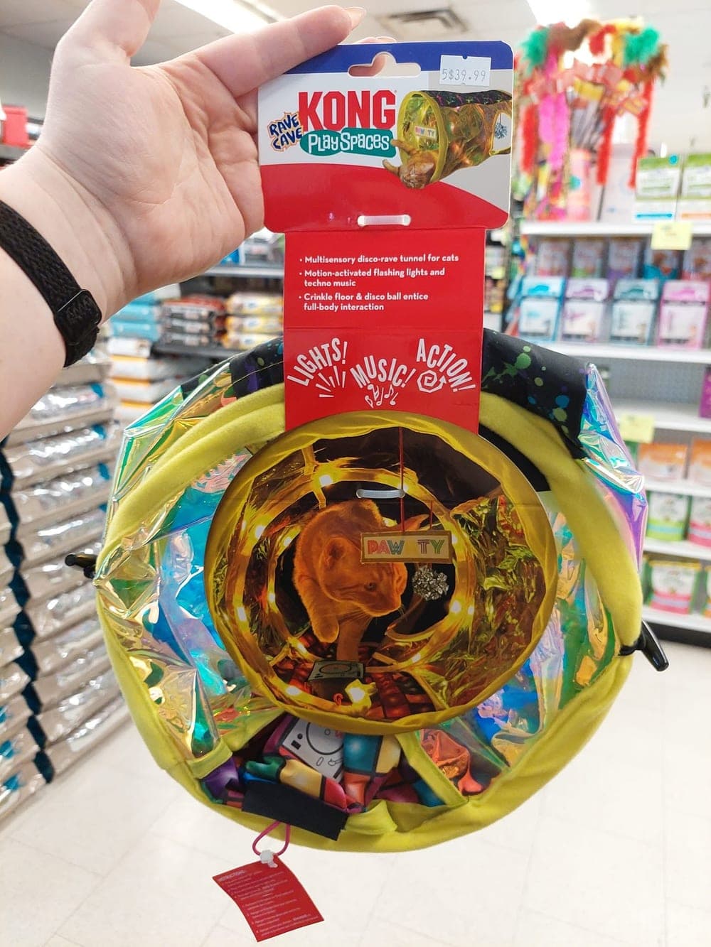 A hand holding up a KONG Play Spaces light-up cat tunnel in the store's cat aisle